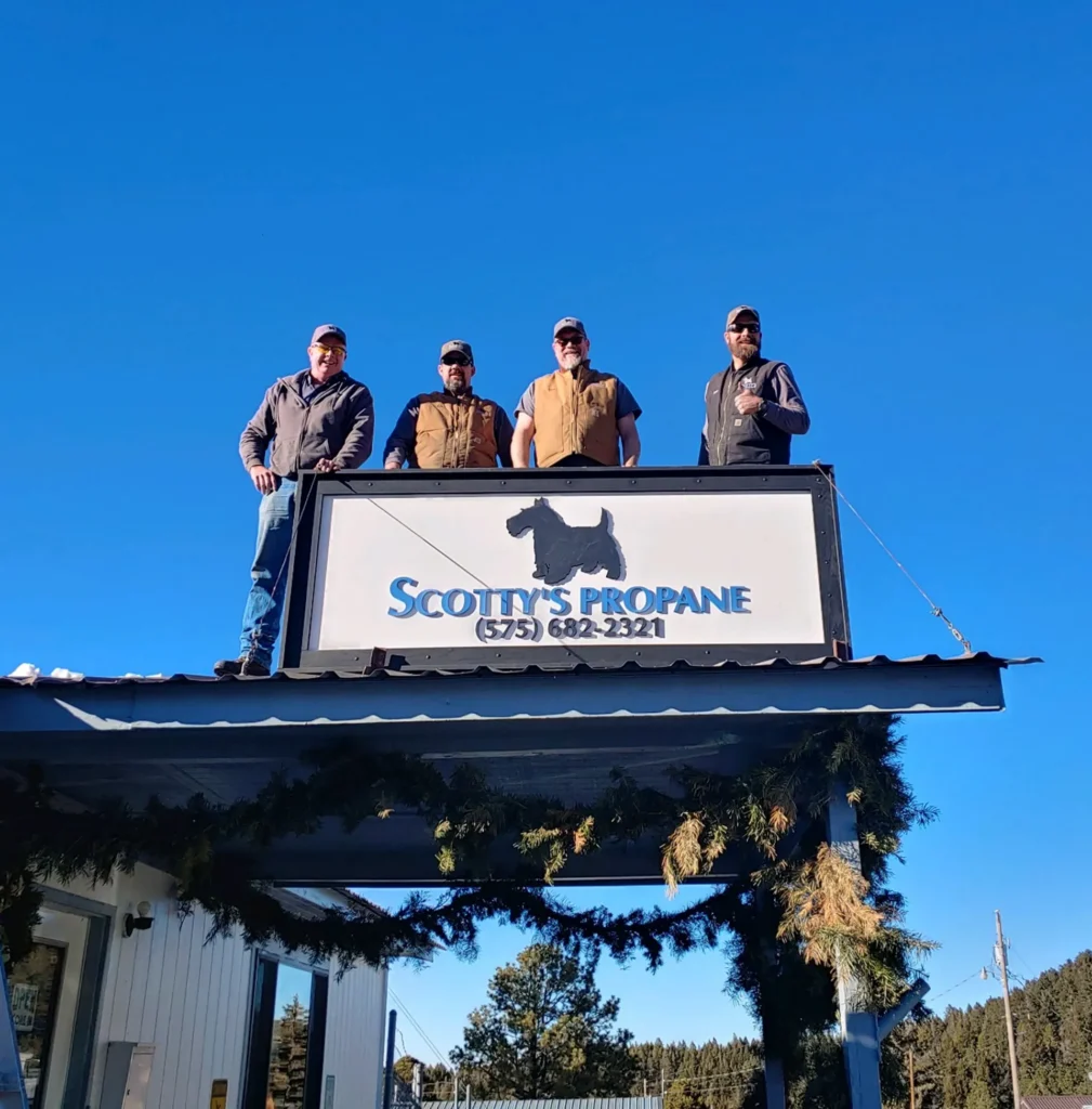 four guys standing on roof over scotty's propane sign